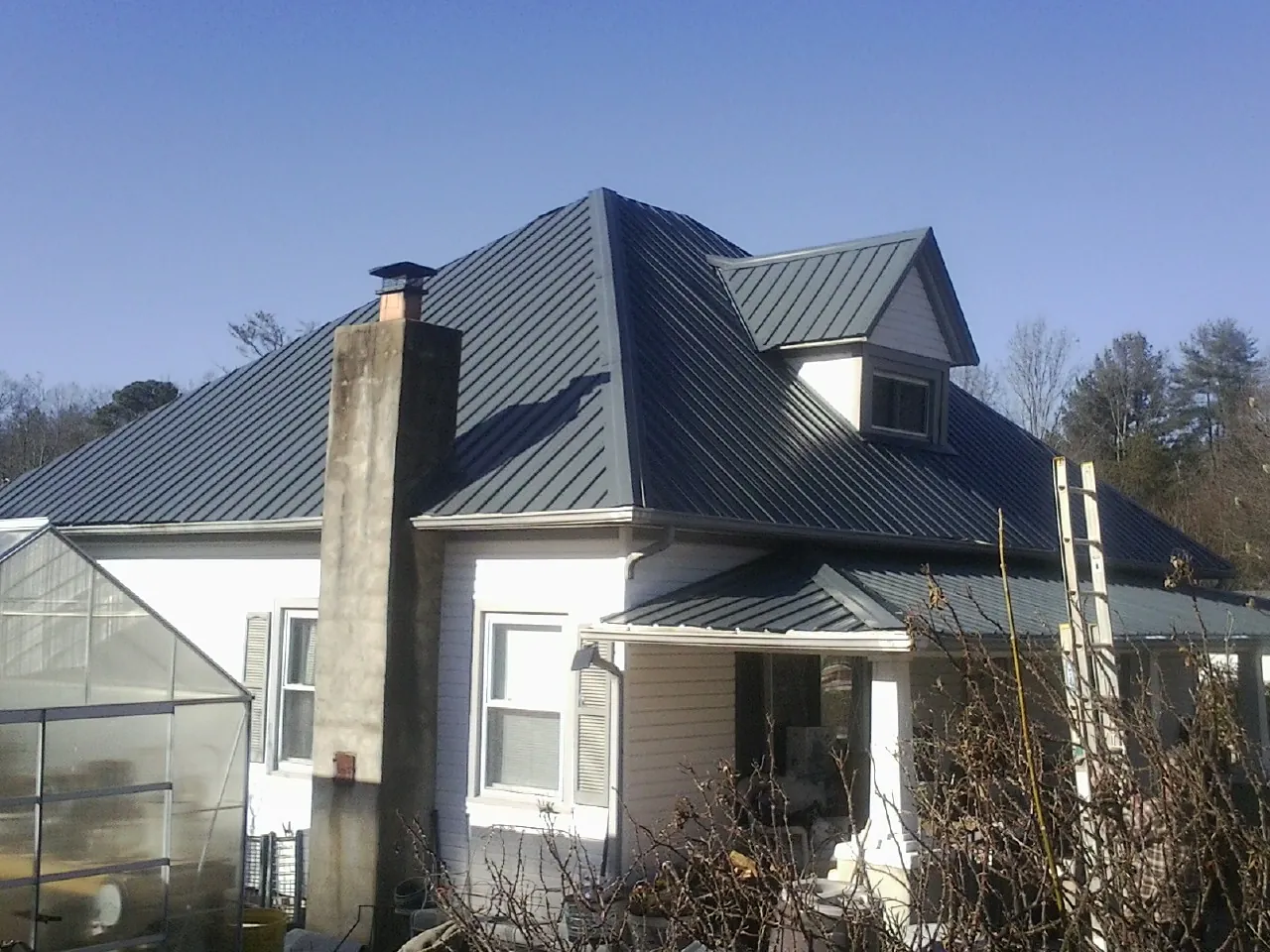 Dark blue standing seam metal roof on a white farmhouse with dormer — Slate & Tile Roof Repair by Roofing Brothers in Shannon City