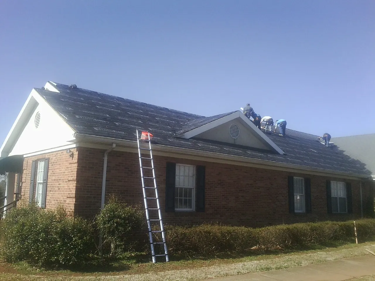 Crew tearing shingles off a brick ranch roof with a ladder set — Metal Roof Repair work by our crew in Shannon City