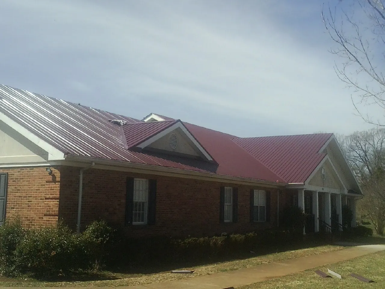 Red metal roof with gabled entries on a long brick building, from a Hail Damage Roof Repair job in Shannon City