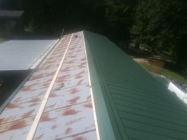 Old rusted panels beside newly installed green metal roofing — Wind Damage Roof Repair by Roofing Brothers in Shannon City