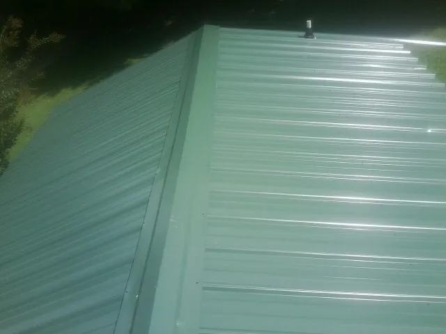 New green metal panels meeting at the ridge of a roof — Flat Roof Repair work by our crew in Shannon City