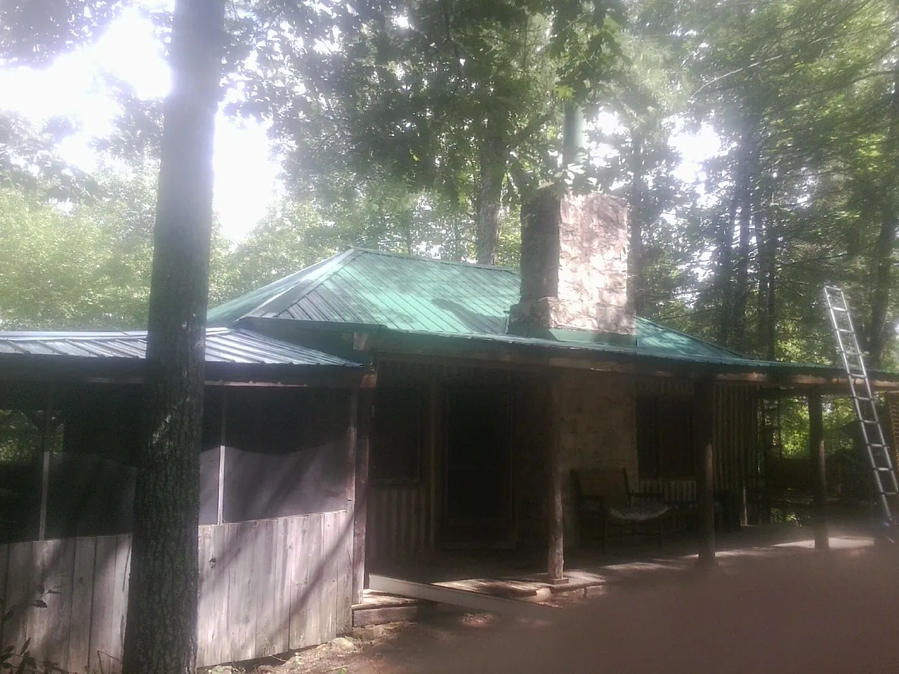 Green metal roof and stone chimney above a log cabin porch in Shannon City