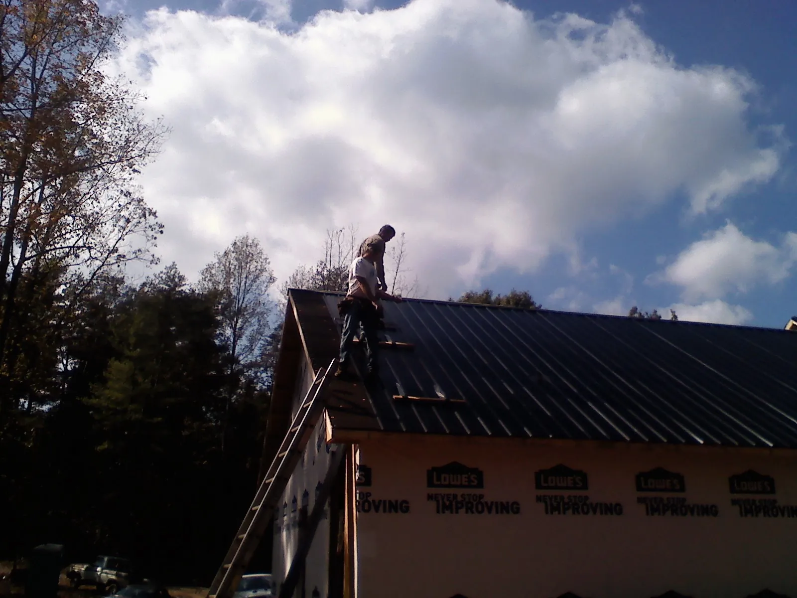Roofer fastening dark metal panels high against a cloudy sky, from a Roof Inspection job in Shannon City