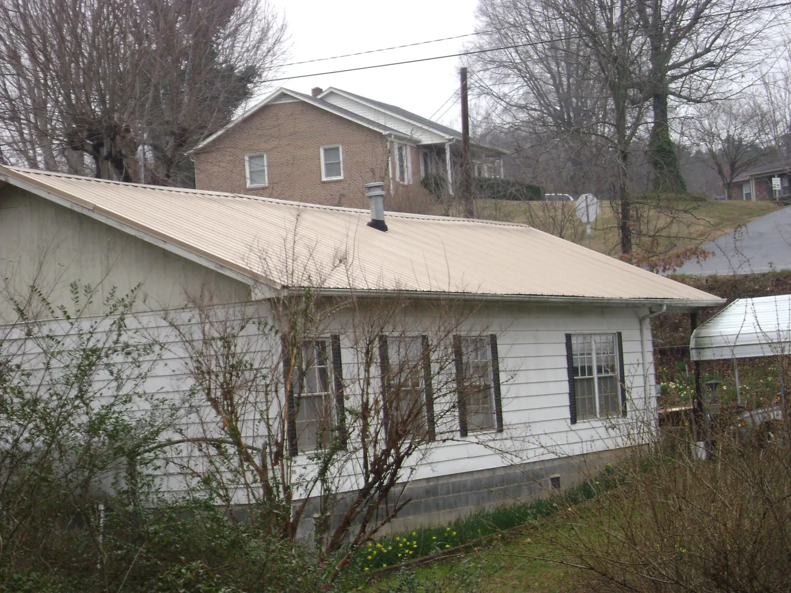 Tan metal roof on a white sided house set into a hillside — Commercial Roofing by Roofing Brothers in Shannon City