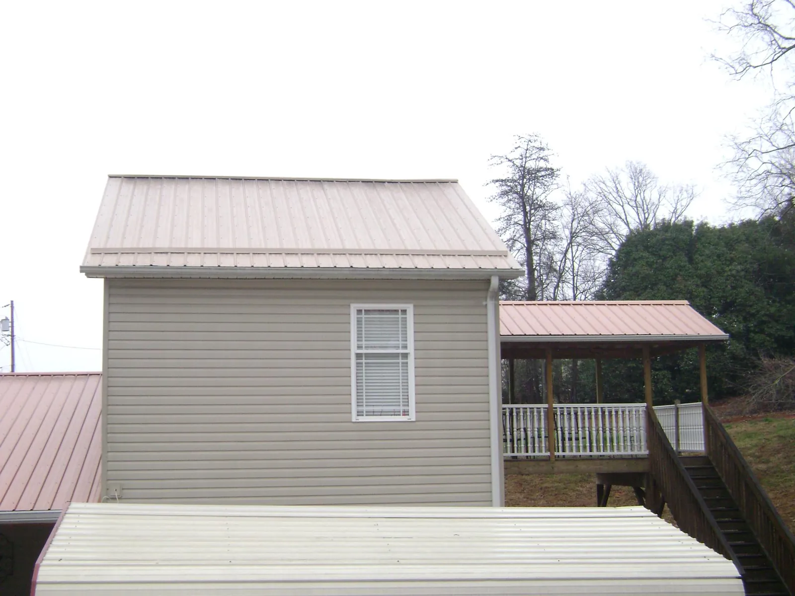 Tan metal roofs on a two story addition and attached porch, from a Roof Replacement job in Shannon City